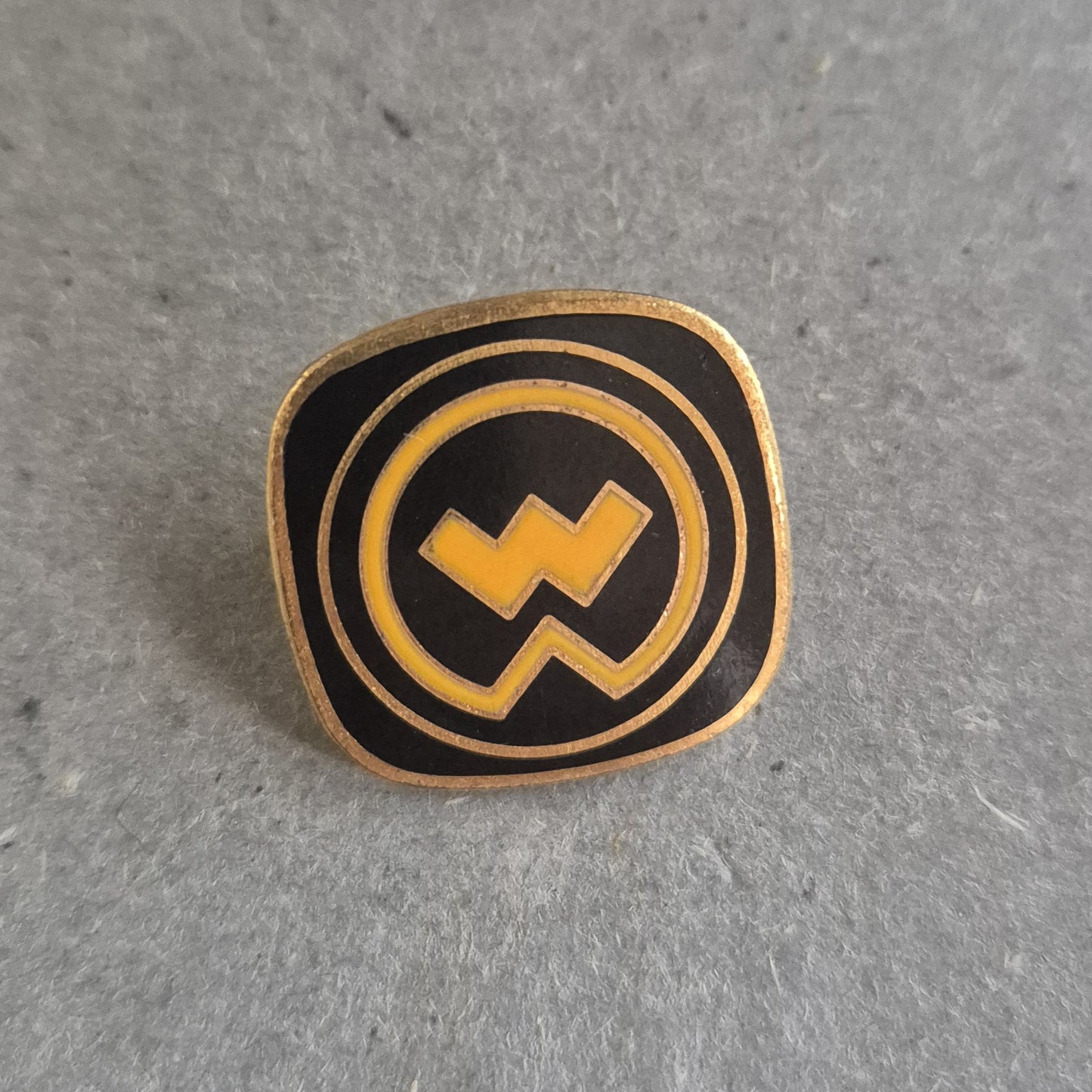 Vintage Emaille-Pin – Schwarzes Logo mit gelbem Blitzsymbol