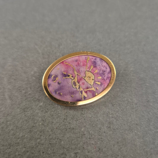 Ovale Brosche mit lila Stoffeinlage und goldener Handzeichnung