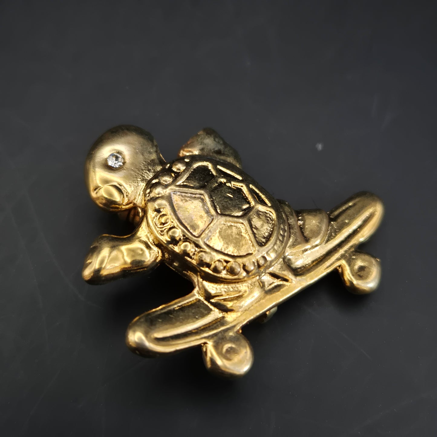 Verspielte Schildkröte auf Skateboard – Goldfarbene Brosche mit Kristall-Auge
