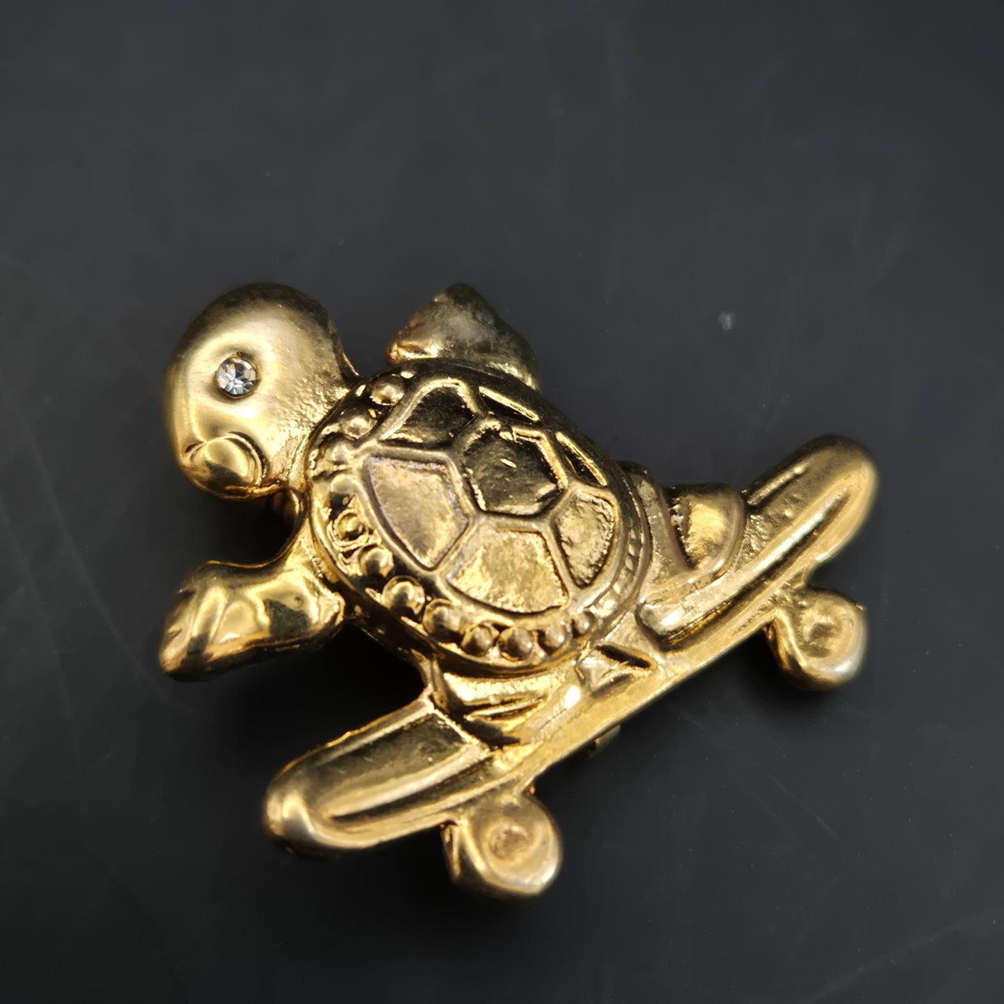 Verspielte Schildkröte auf Skateboard – Goldfarbene Brosche mit Kristall-Auge