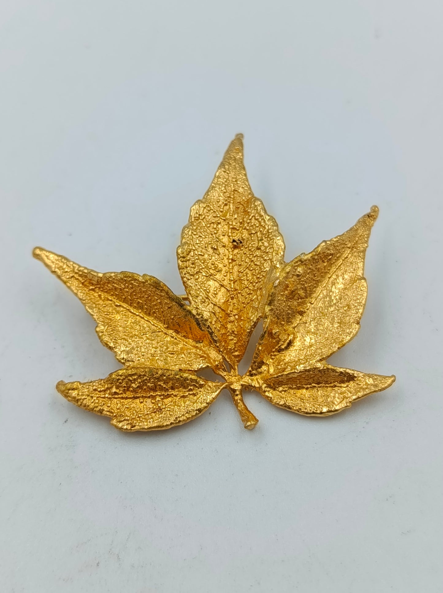 Goldfarbene Brosche in Blattform mit strukturierter Oberfläche