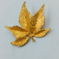 Goldfarbene Brosche in Blattform mit strukturierter Oberfläche