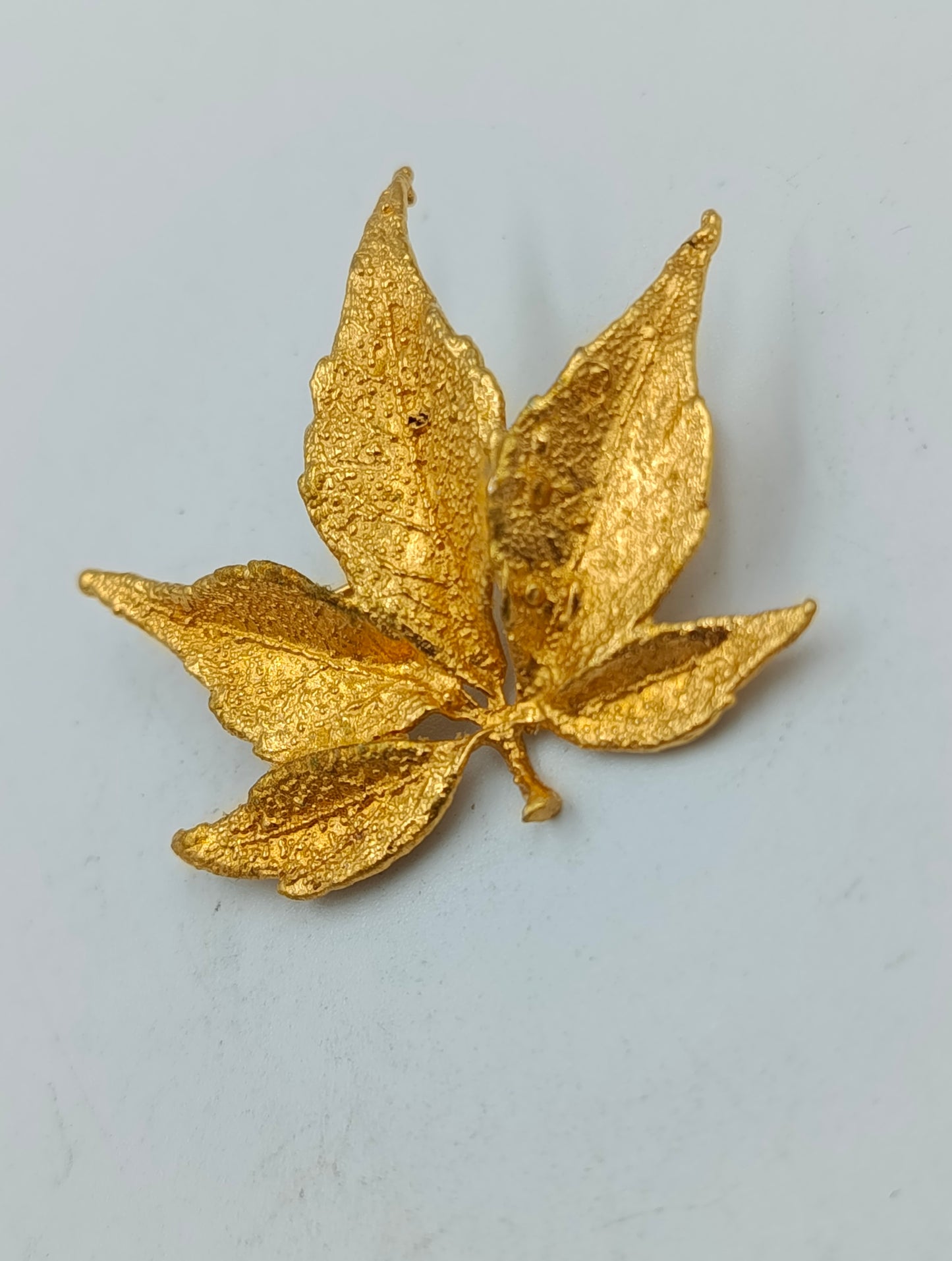 Goldfarbene Brosche in Blattform mit strukturierter Oberfläche