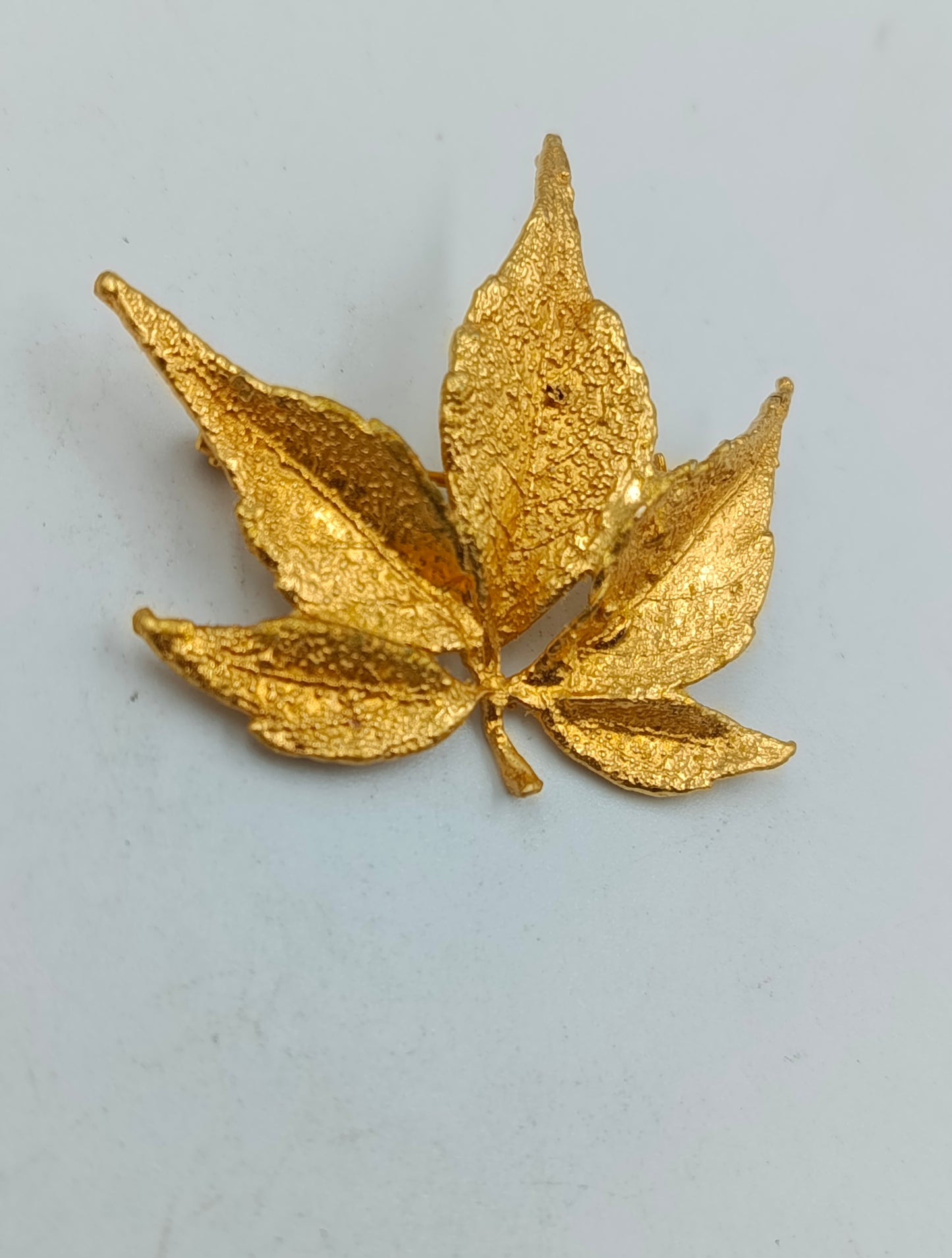 Goldfarbene Brosche in Blattform mit strukturierter Oberfläche