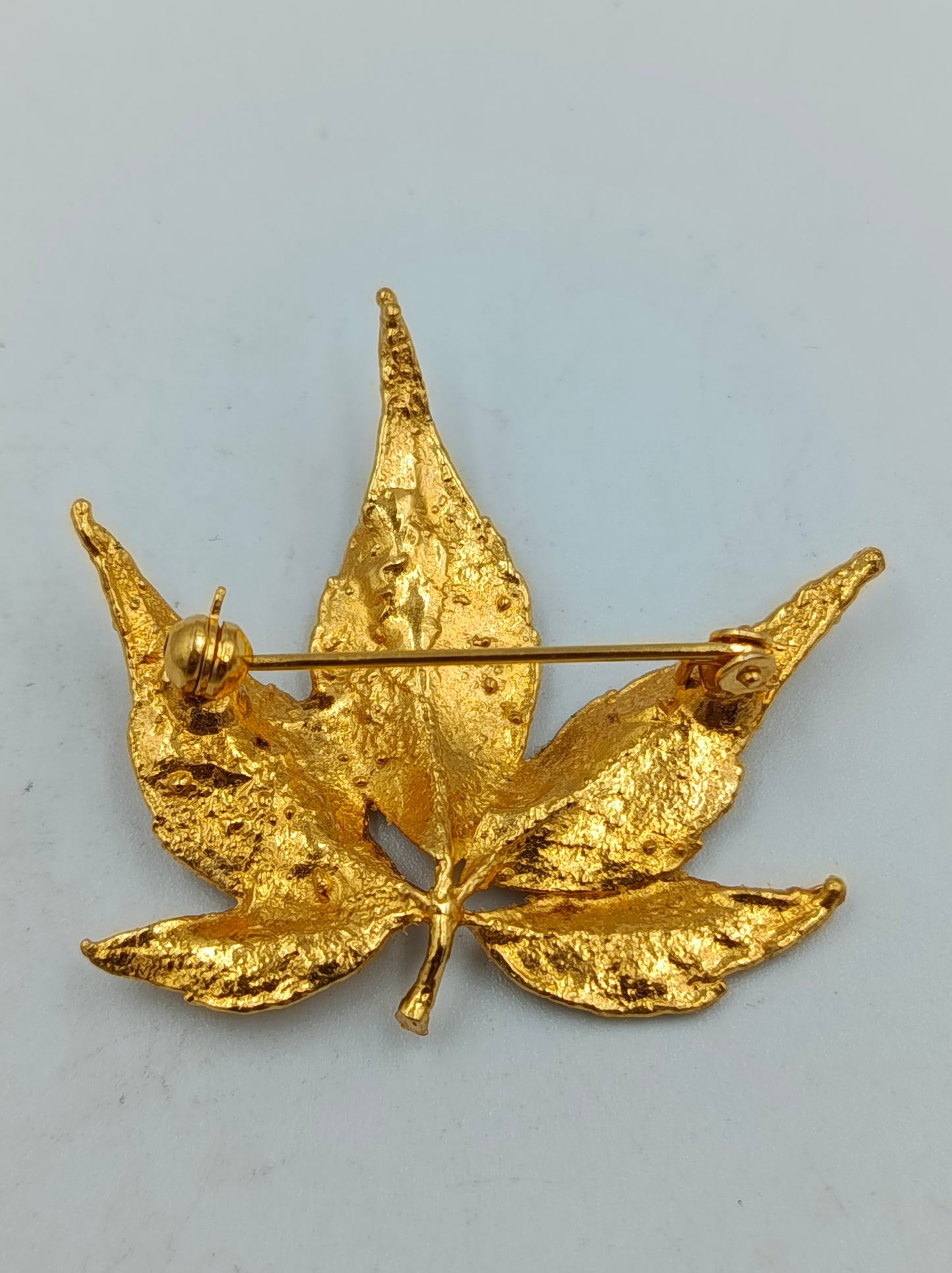 Goldfarbene Brosche in Blattform mit strukturierter Oberfläche