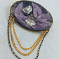 Ovale Brosche mit violettem Blattmotiv und goldfarbenen Zierketten