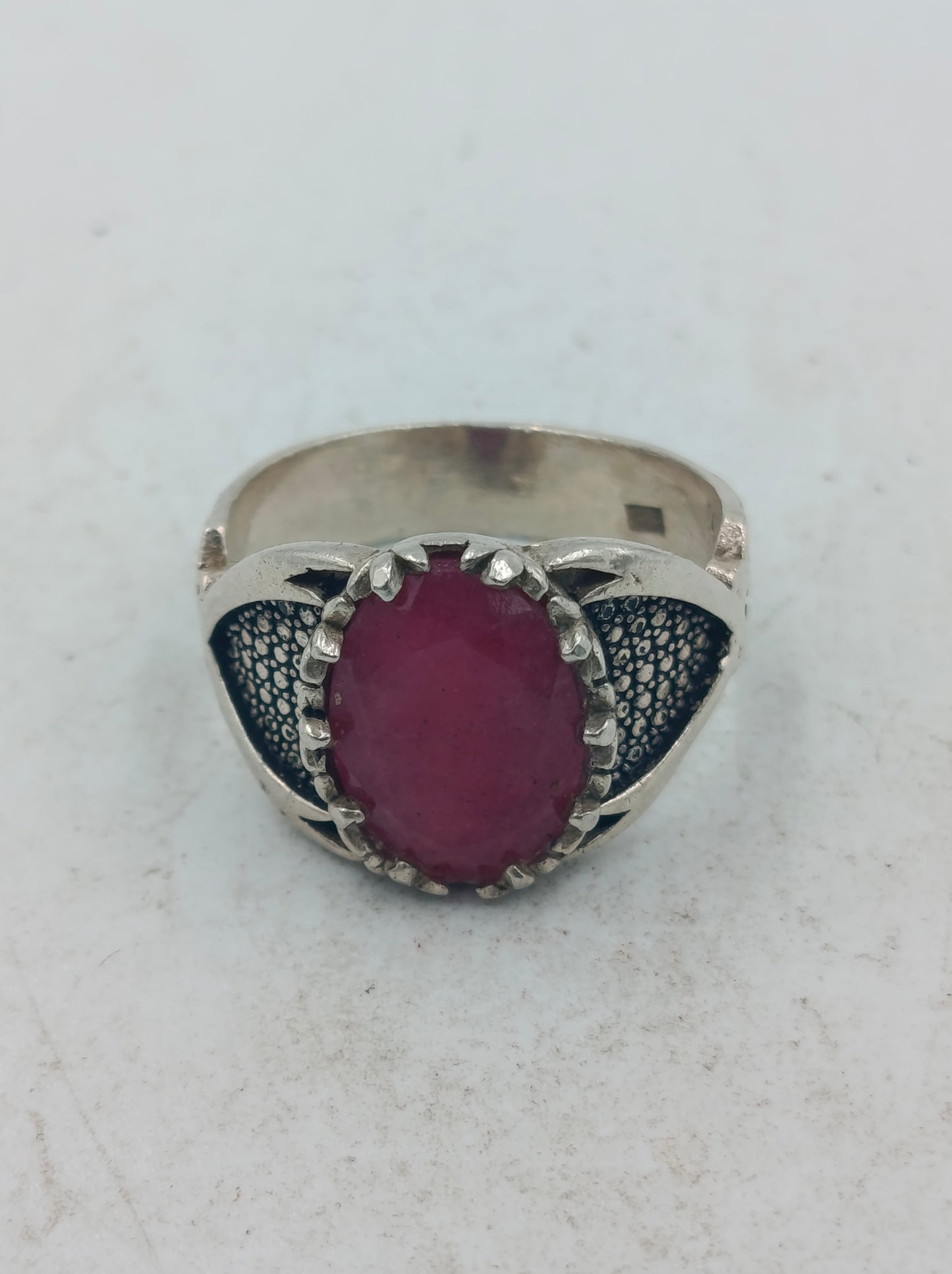Silberring mit grossem rubinfarbenem Stein und kunstvoll verzierten Seitenflaechen im edlen Stil