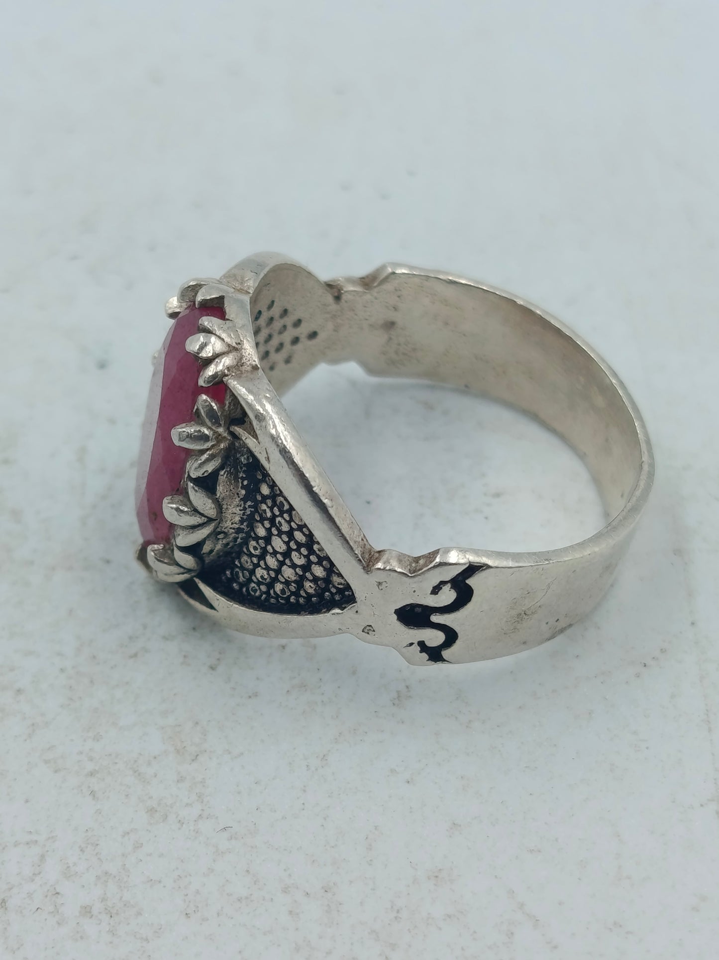Silberring mit grossem rubinfarbenem Stein und kunstvoll verzierten Seitenflaechen im edlen Stil