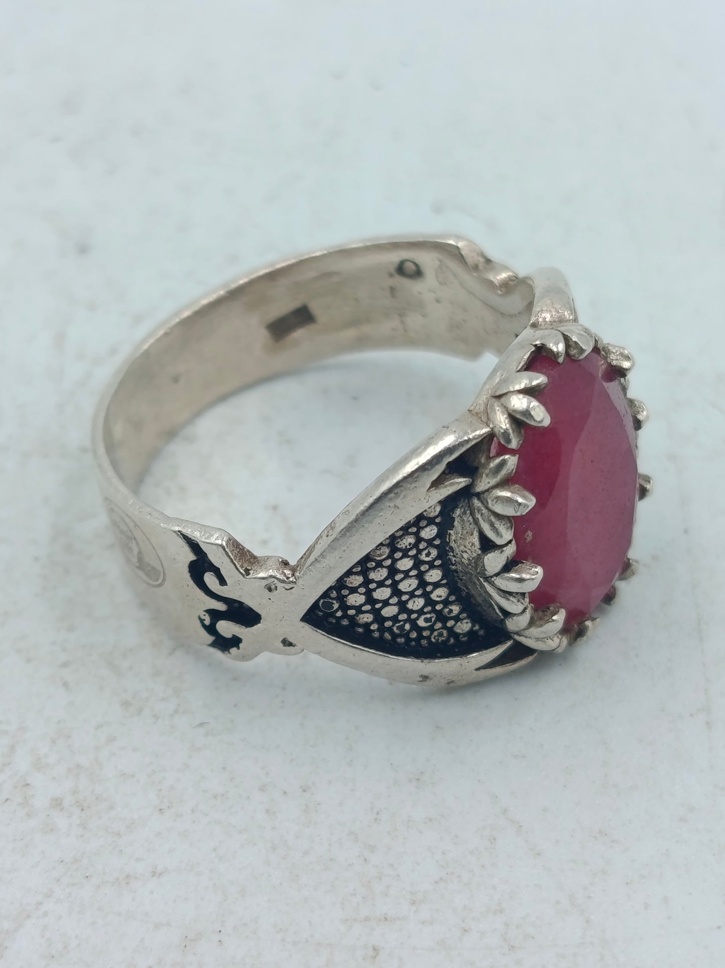 Silberring mit grossem rubinfarbenem Stein und kunstvoll verzierten Seitenflaechen im edlen Stil