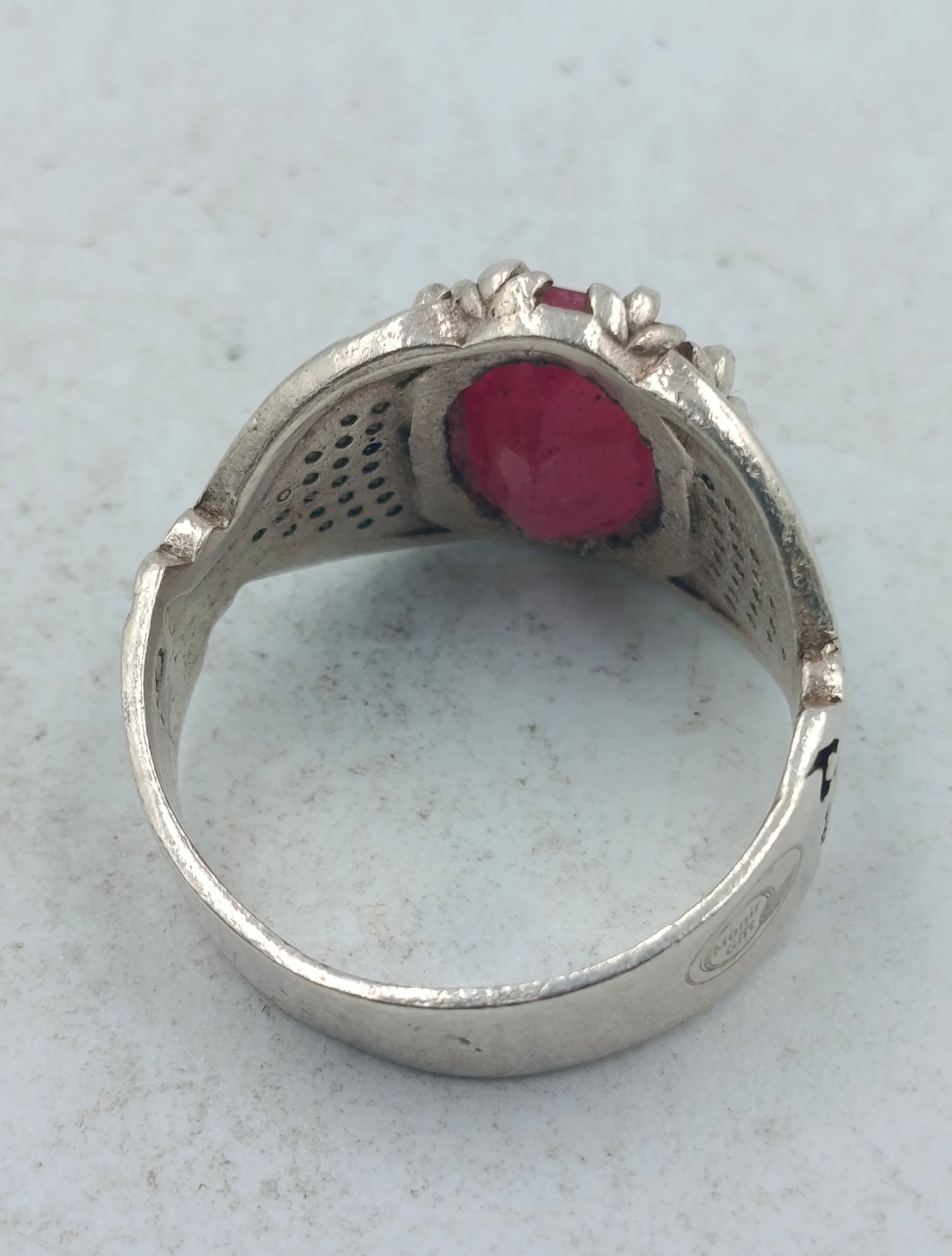 Silberring mit grossem rubinfarbenem Stein und kunstvoll verzierten Seitenflaechen im edlen Stil