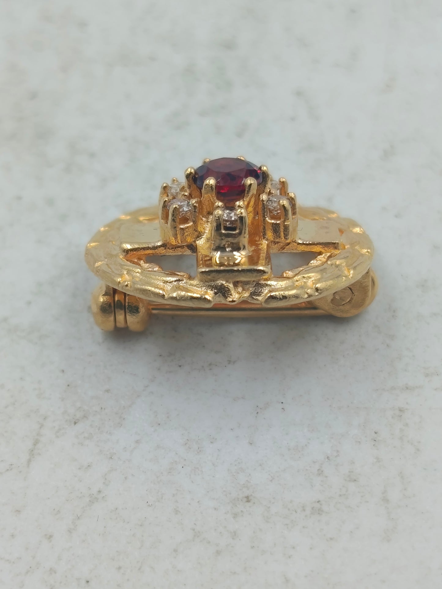 Goldfarbene Brosche mit rotem Mittelstein und funkelnden Akzenten im klassischen Stil