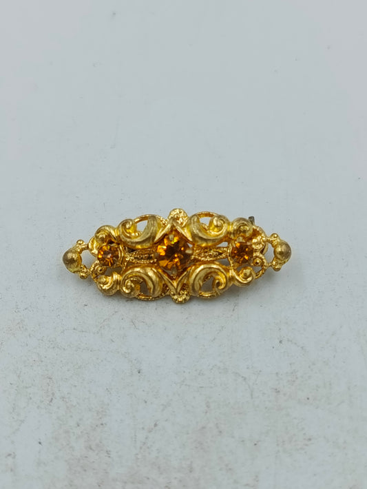 Goldfarbene Brosche mit filigranem Ornamentdesign und funkelnden Steinen