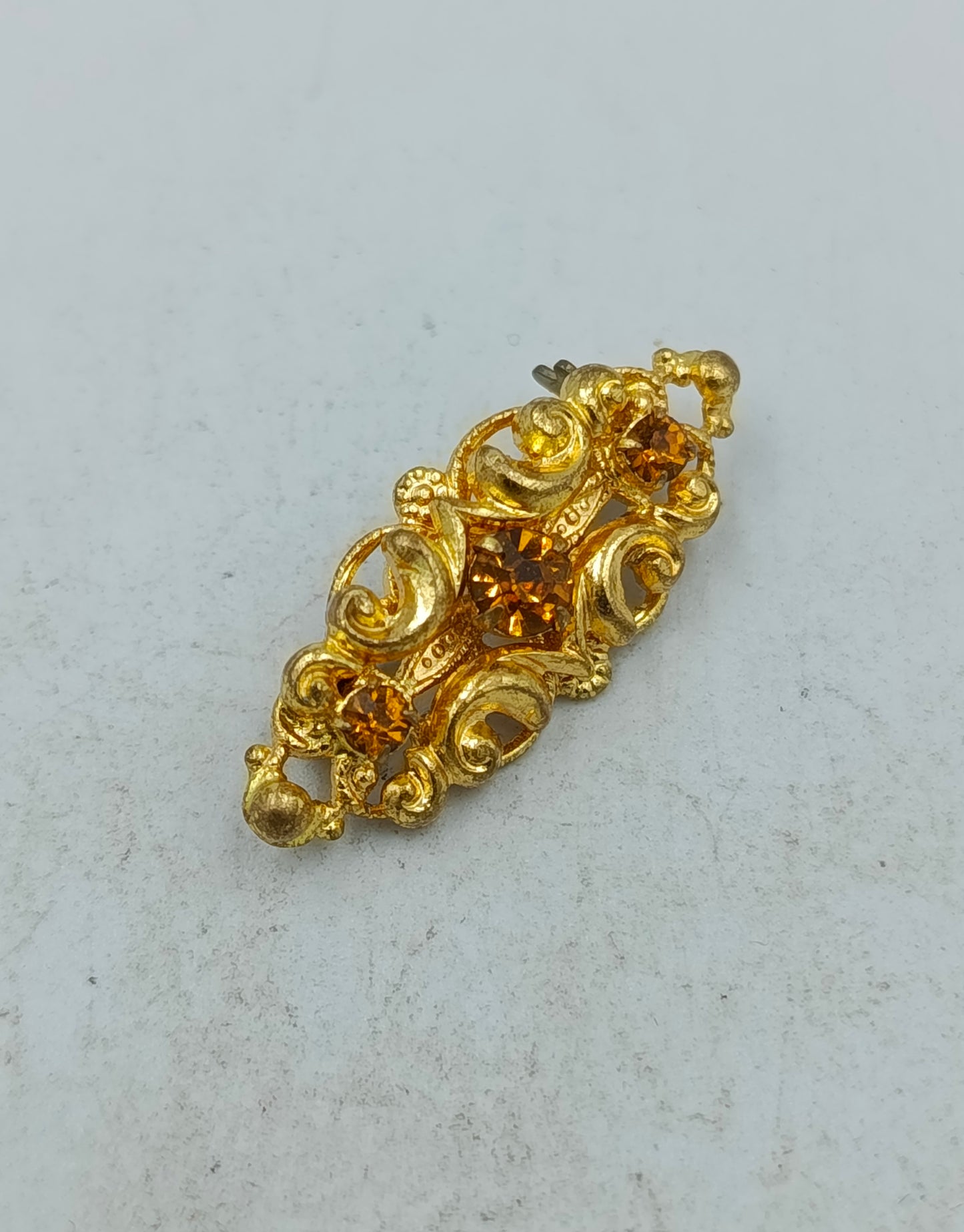 Goldfarbene Brosche mit filigranem Ornamentdesign und funkelnden Steinen