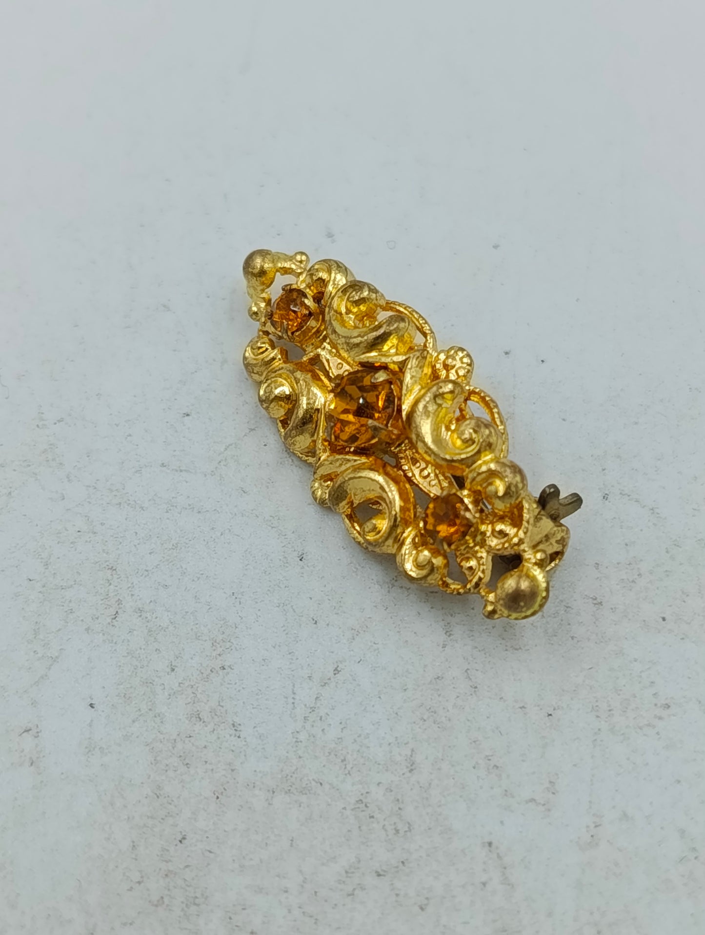 Goldfarbene Brosche mit filigranem Ornamentdesign und funkelnden Steinen