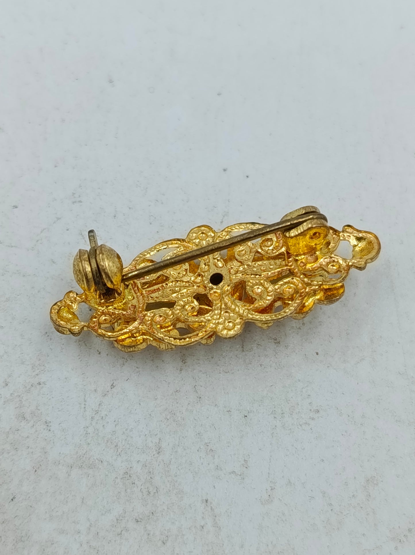 Goldfarbene Brosche mit filigranem Ornamentdesign und funkelnden Steinen