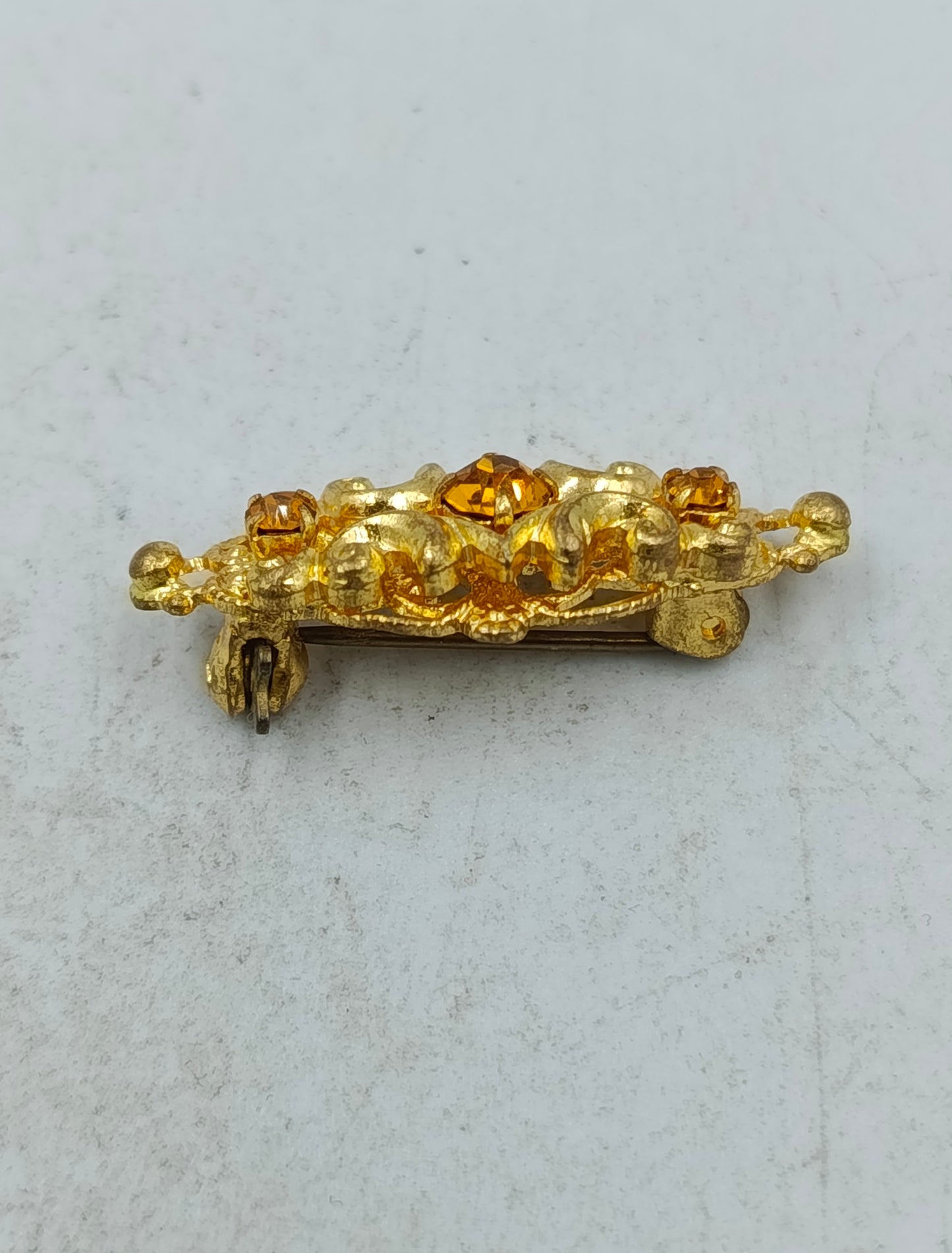 Goldfarbene Brosche mit filigranem Ornamentdesign und funkelnden Steinen