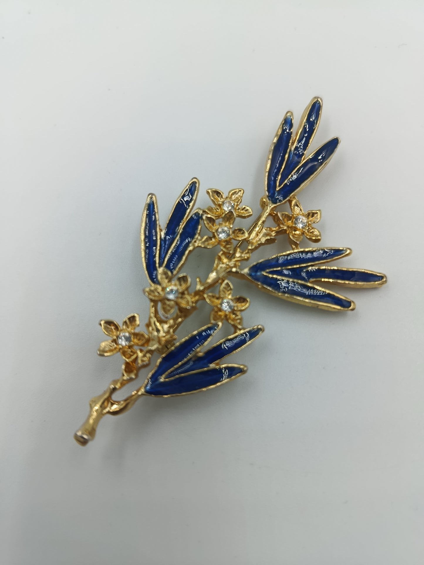 Elegante Brosche mit blauen Emailleblättern und funkelnden Blüten in Goldoptik