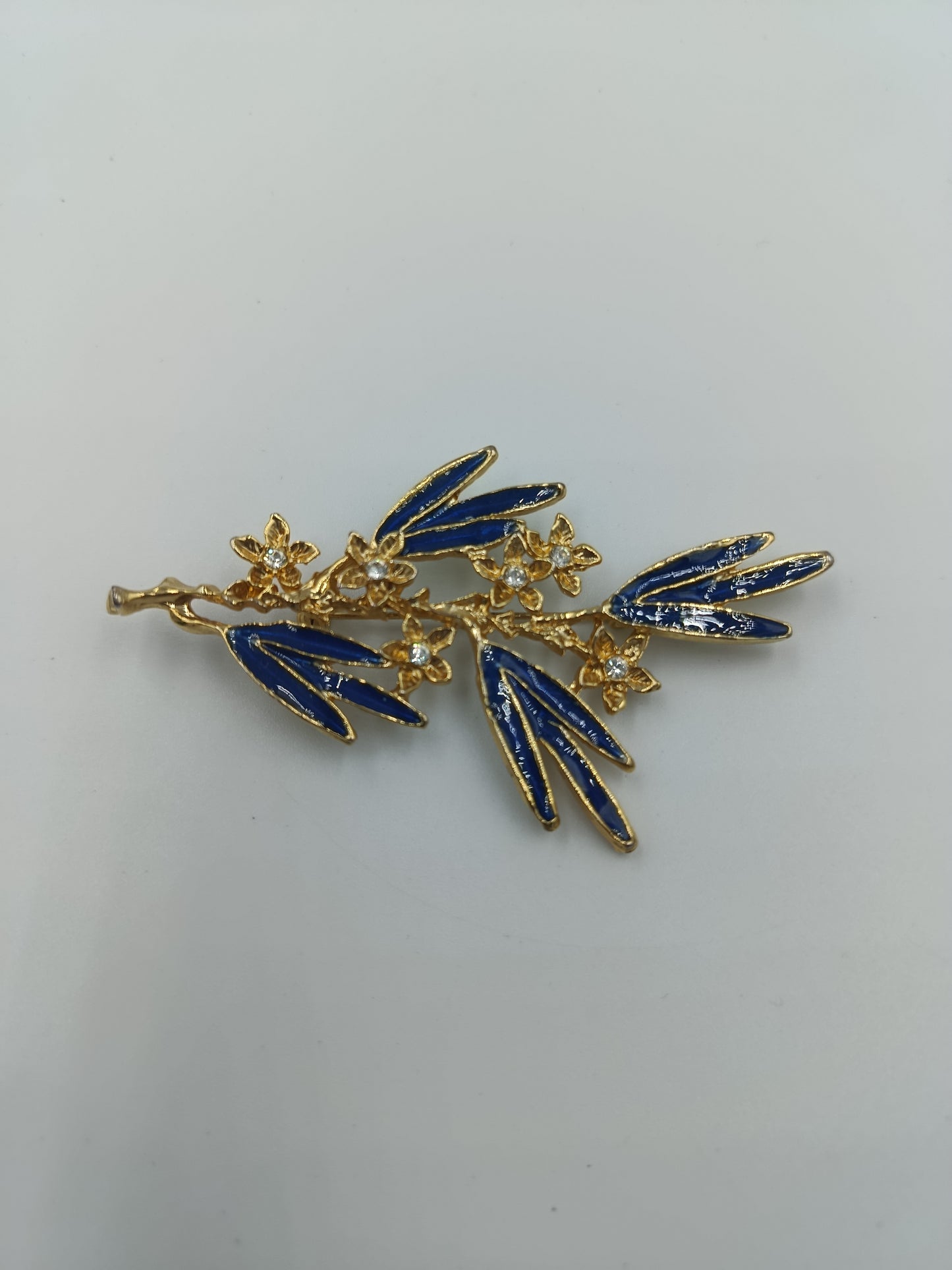 Elegante Brosche mit blauen Emailleblättern und funkelnden Blüten in Goldoptik