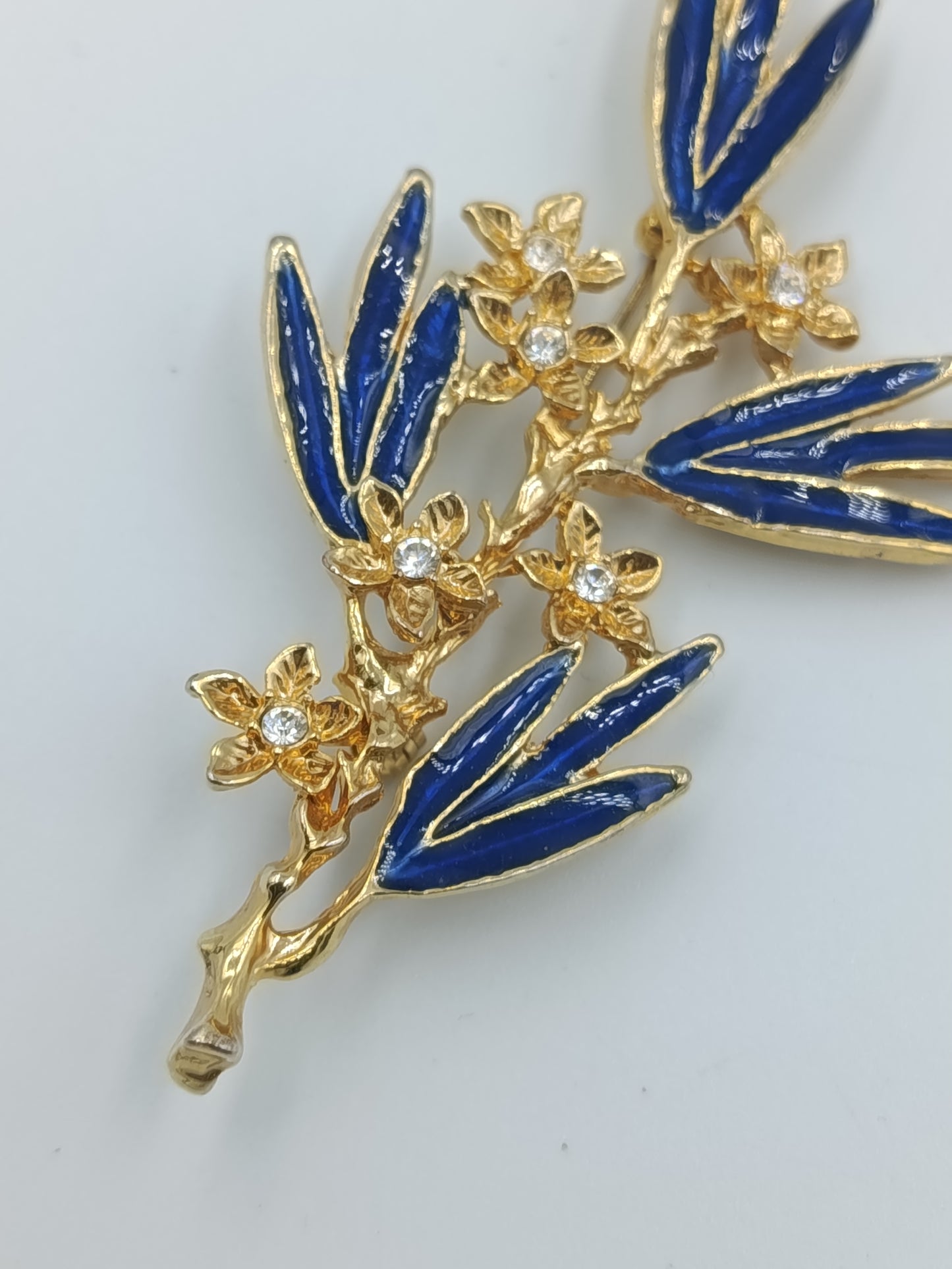 Elegante Brosche mit blauen Emailleblättern und funkelnden Blüten in Goldoptik